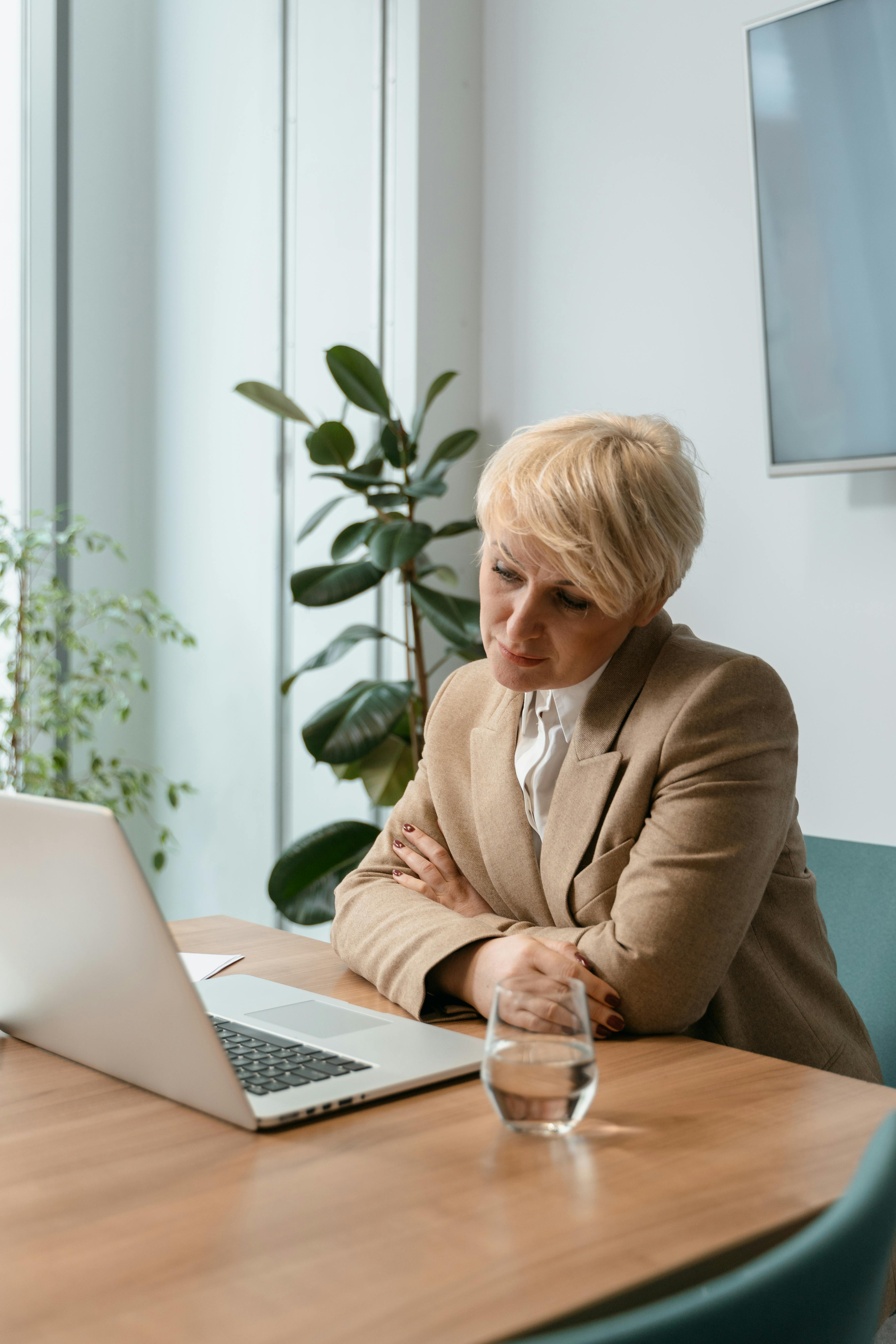 Professional woman in a blazer working seriously on a laptop in an office setting.