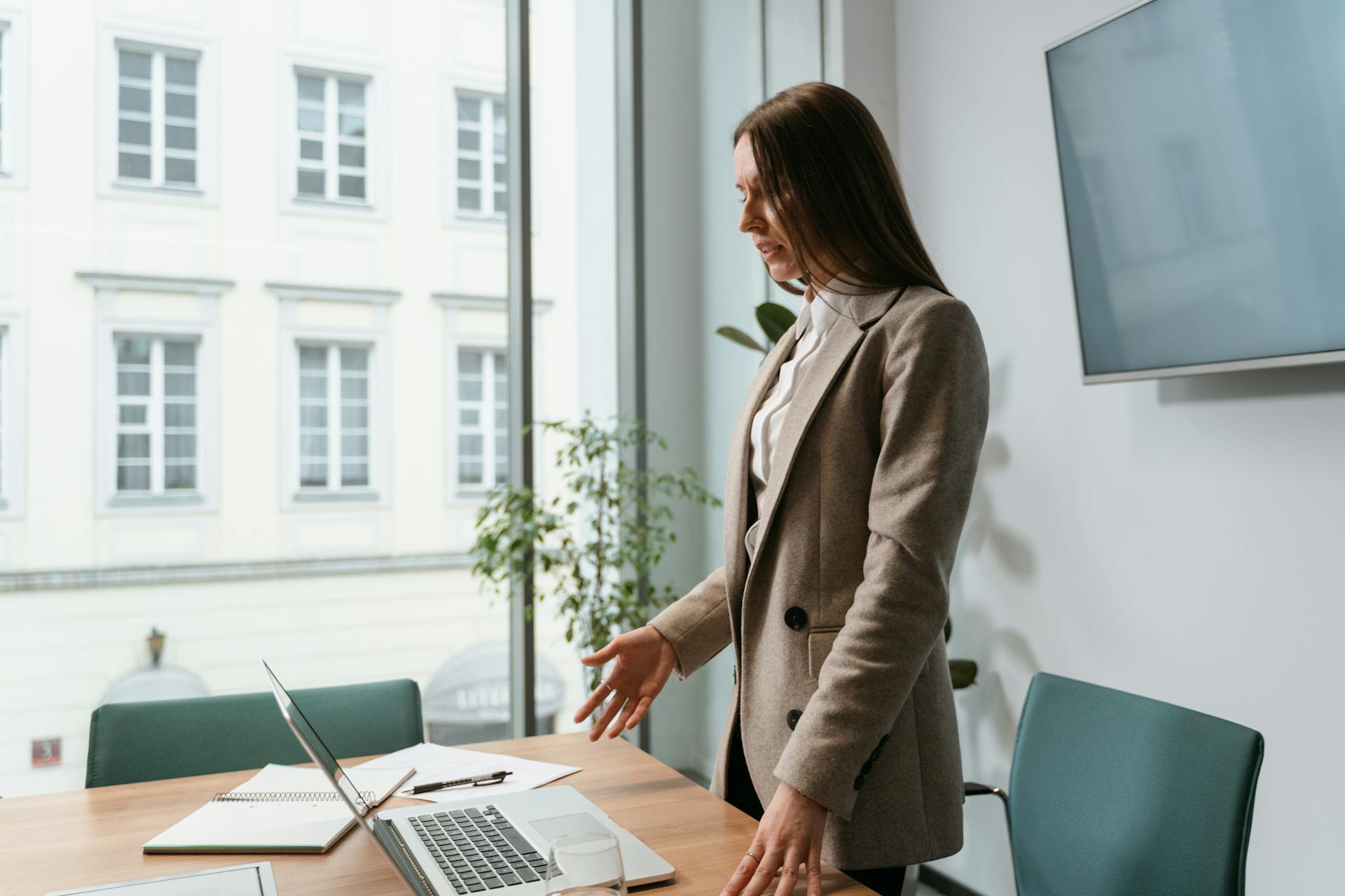 Professional woman in an office setting working on a laptop near a window.