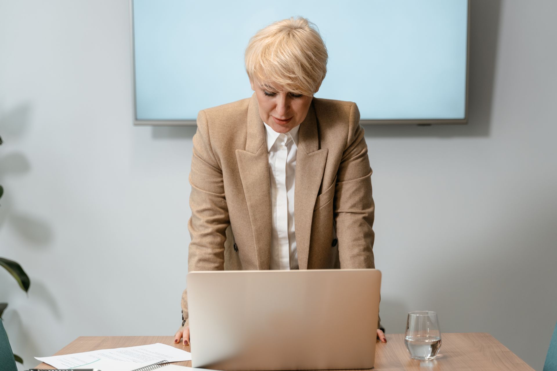 A determined businesswoman with short blonde hair focuses on her laptop in a modern office.