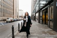 Confident businesswoman walking down city street holding coffee, showcasing modern city lifestyle.
