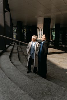 Two businesswomen in formal attire standing on steps outdoors, smiling.