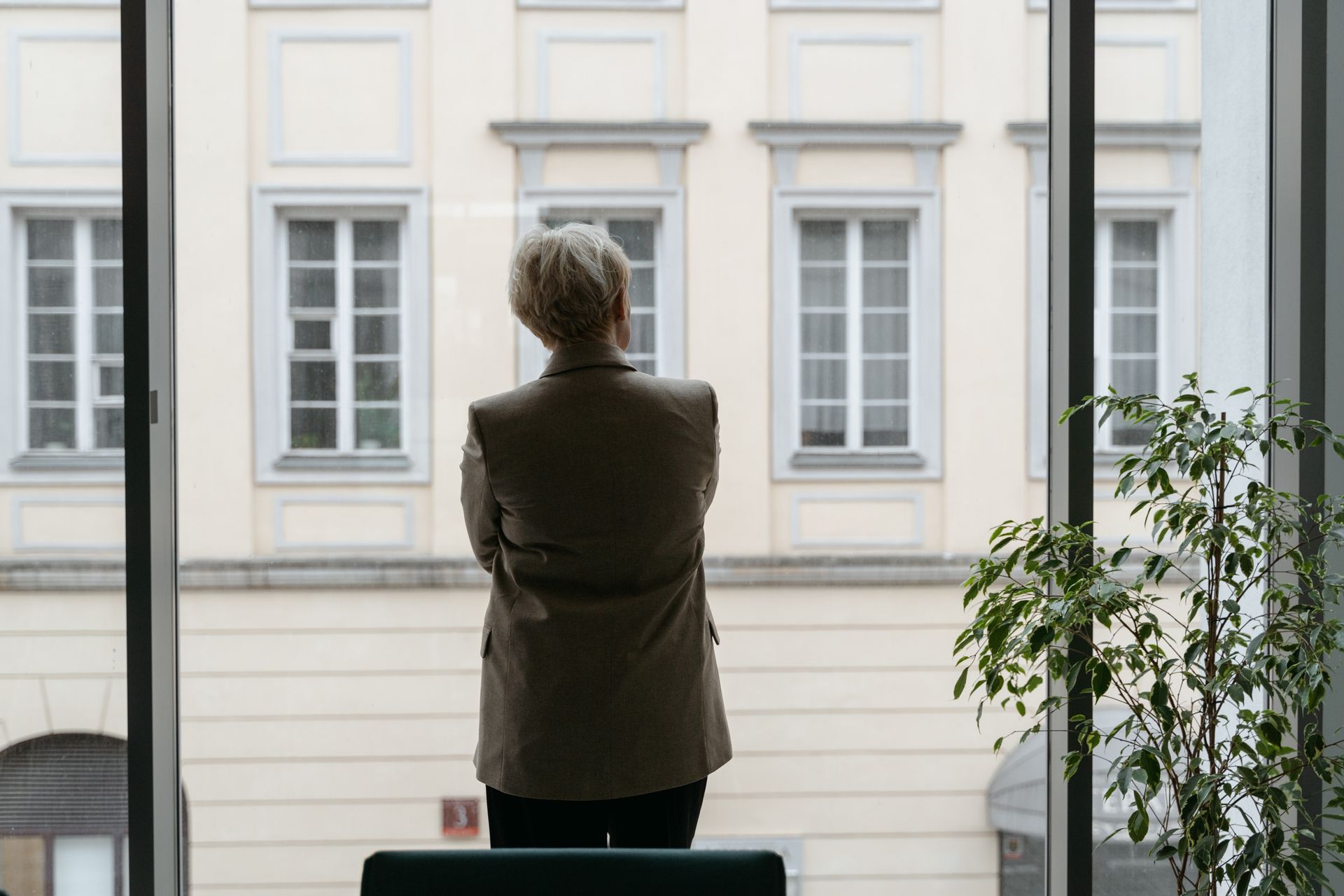 A professional woman gazes thoughtfully through an office window, lost in contemplation.