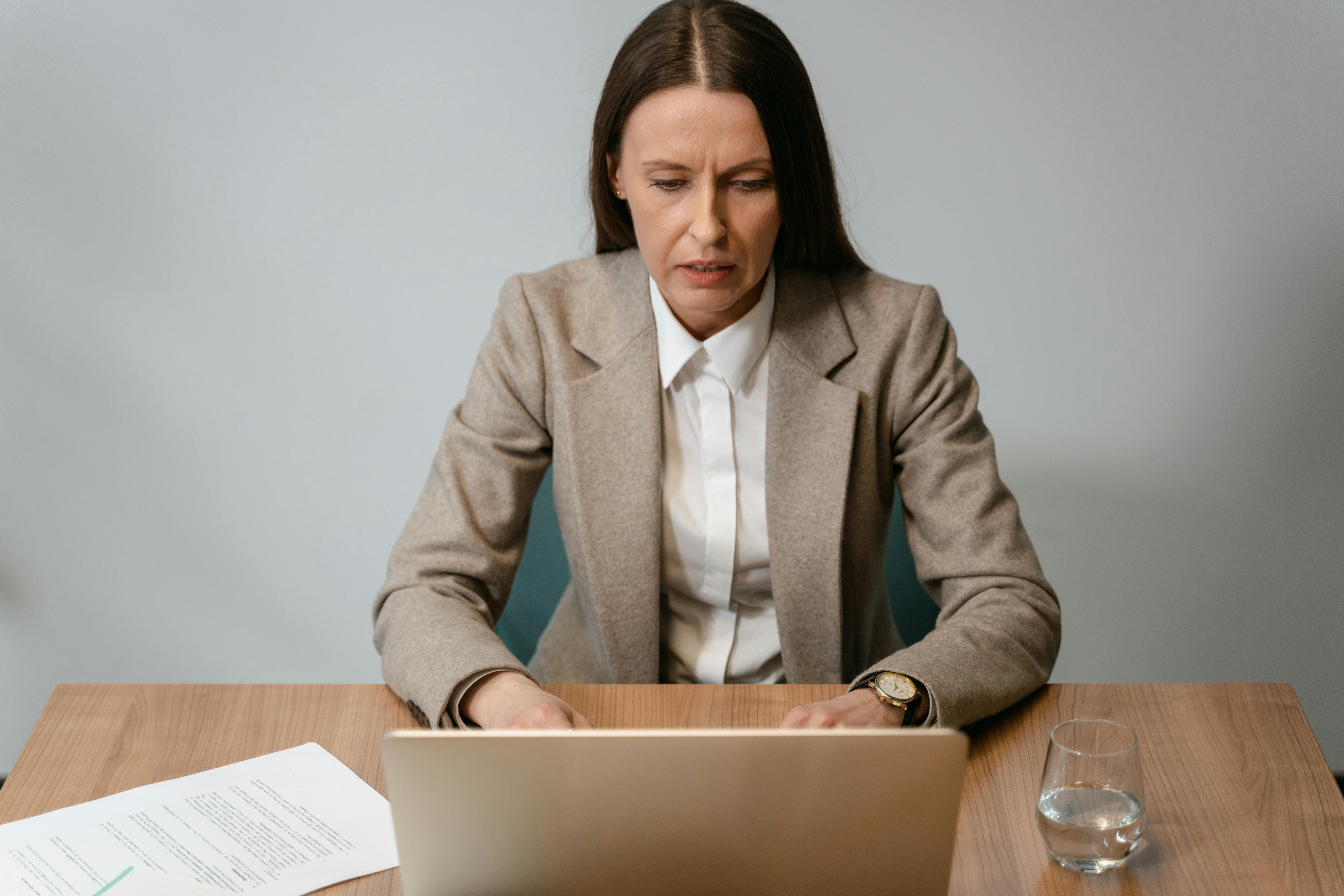 a woman in a brown blazer working on her laptop