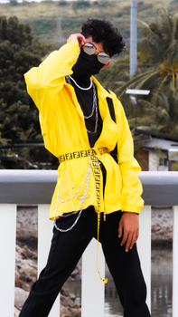 Stylish young man in vibrant yellow outfit posing outdoors with sunglasses and mask.