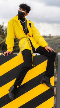 A stylish model poses in a yellow jacket and mask with a scenic outdoor backdrop.