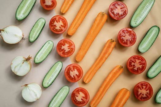 Top view of fresh sliced vegetables including carrots, cucumbers, onions, and tomatoes in a flat lay design.