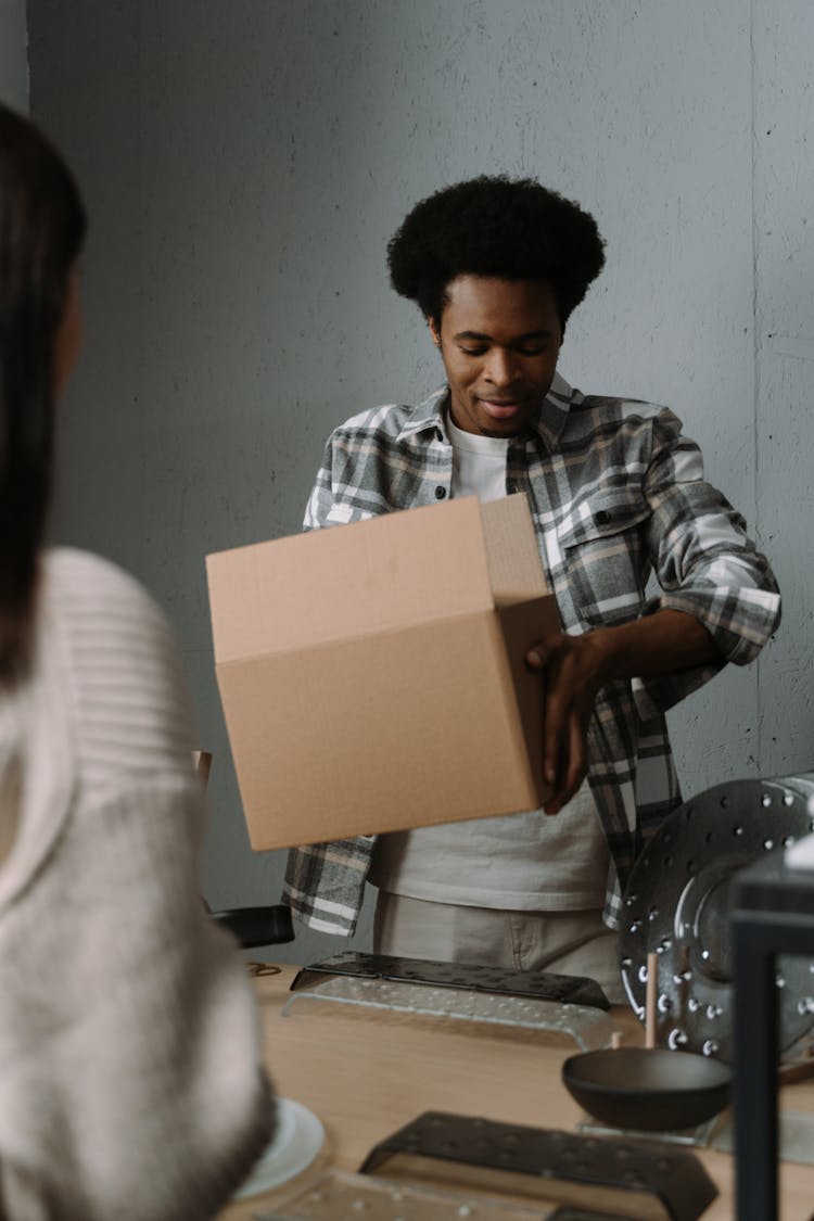 Man In A Plaid Shirt Holding A Brown Box