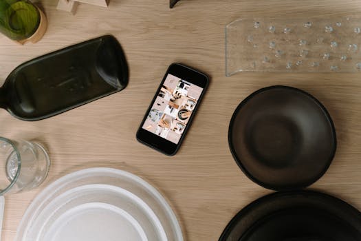 Modern flat lay featuring a smartphone on a wooden table surrounded by dishes and objects.