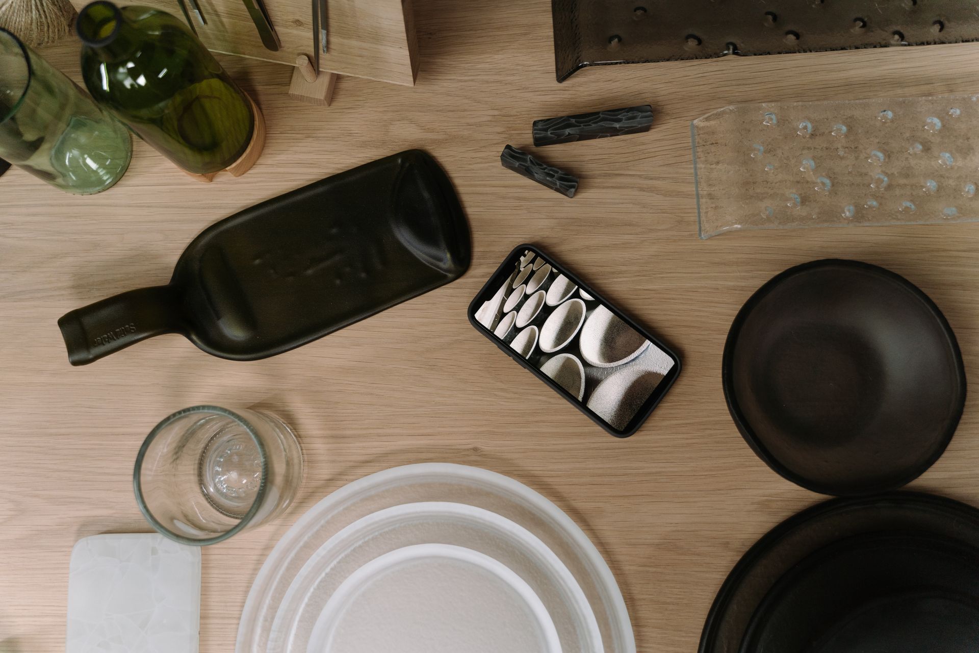 A flat lay arrangement of glass bottles and a smartphone on a wooden table, displaying a bowl pattern.