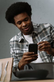 African American man using smartphone in contemporary kitchen, focused on technology.