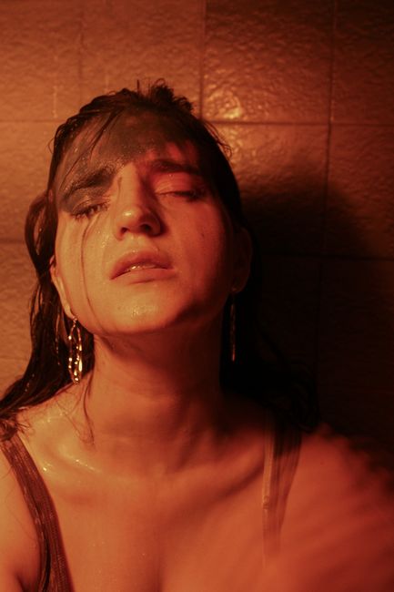 Young mindful female with makeup on eyelid and closed eyes against ceramic wall in bathroom