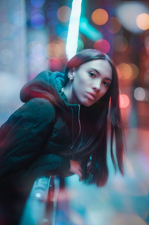 Free Artistic portrait of a woman in hoodie with colorful bokeh lights at night. Stock Photo