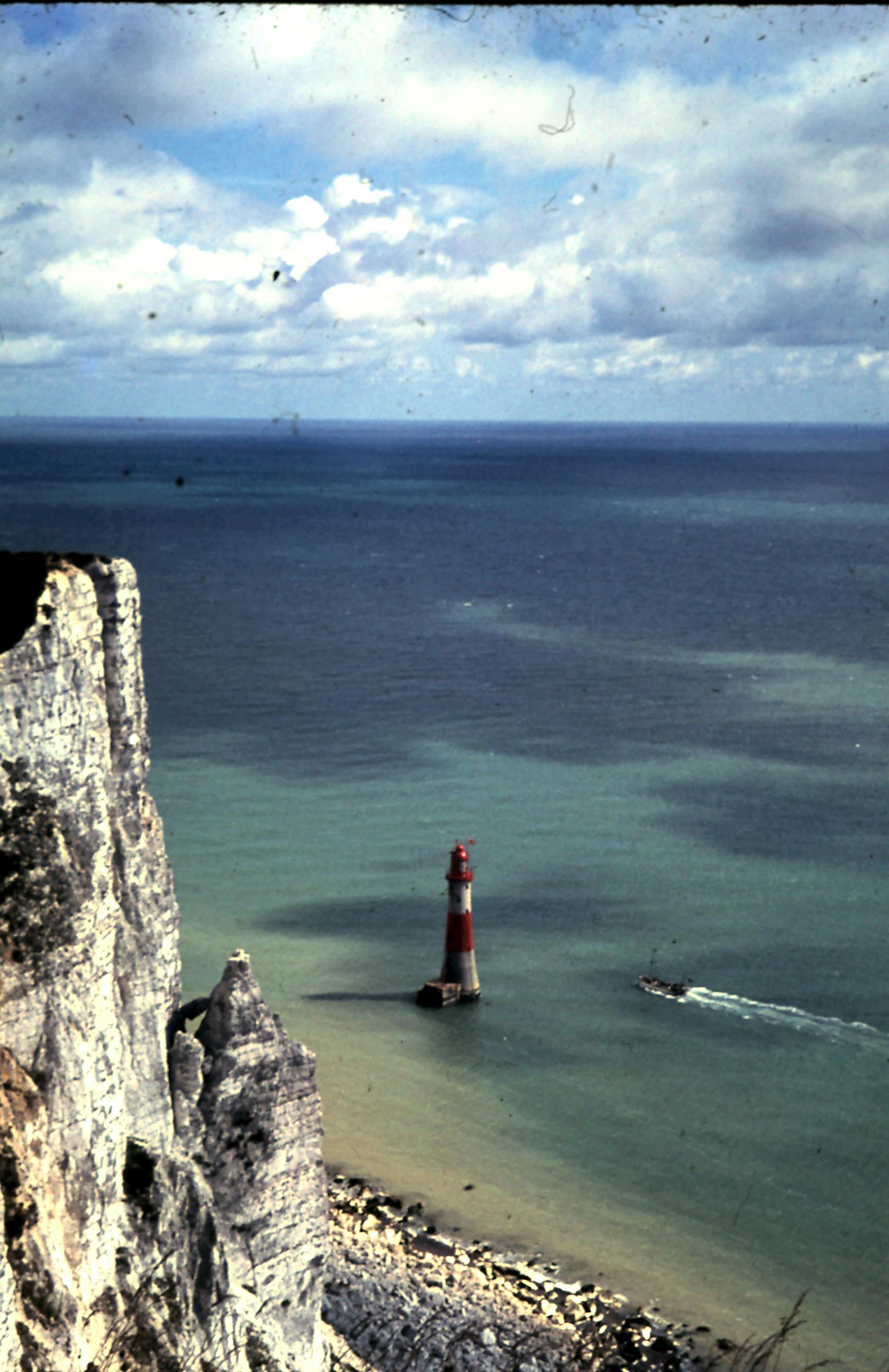 Breathtaking aerial view of Beachy Head Lighthouse and cliffs against the vast ocean under a cloudy sky.