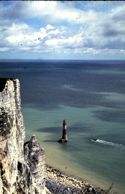 Breathtaking aerial view of Beachy Head Lighthouse and cliffs against the vast ocean under a cloudy sky.