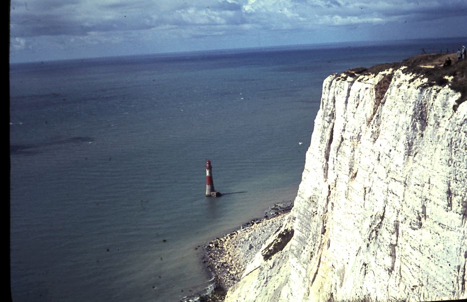Dramatic shot of Beachy Head Lighthouse against towering white cliffs and vast sea.