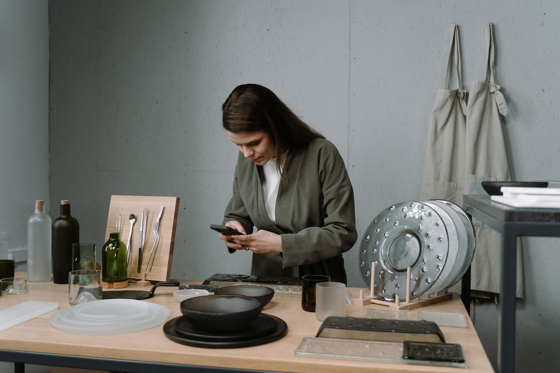 Craftswoman using a smartphone to capture her handmade ceramic creations in a modern studio.