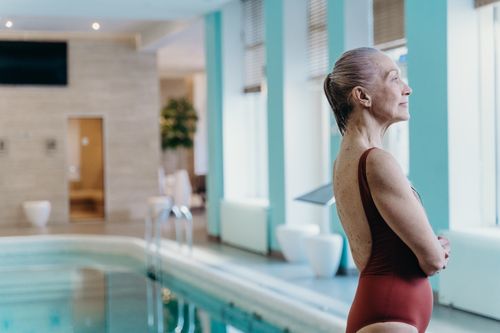 Free Elderly woman wearing swimsuit standing by an indoor pool. Calm and contemplative. Stock Photo