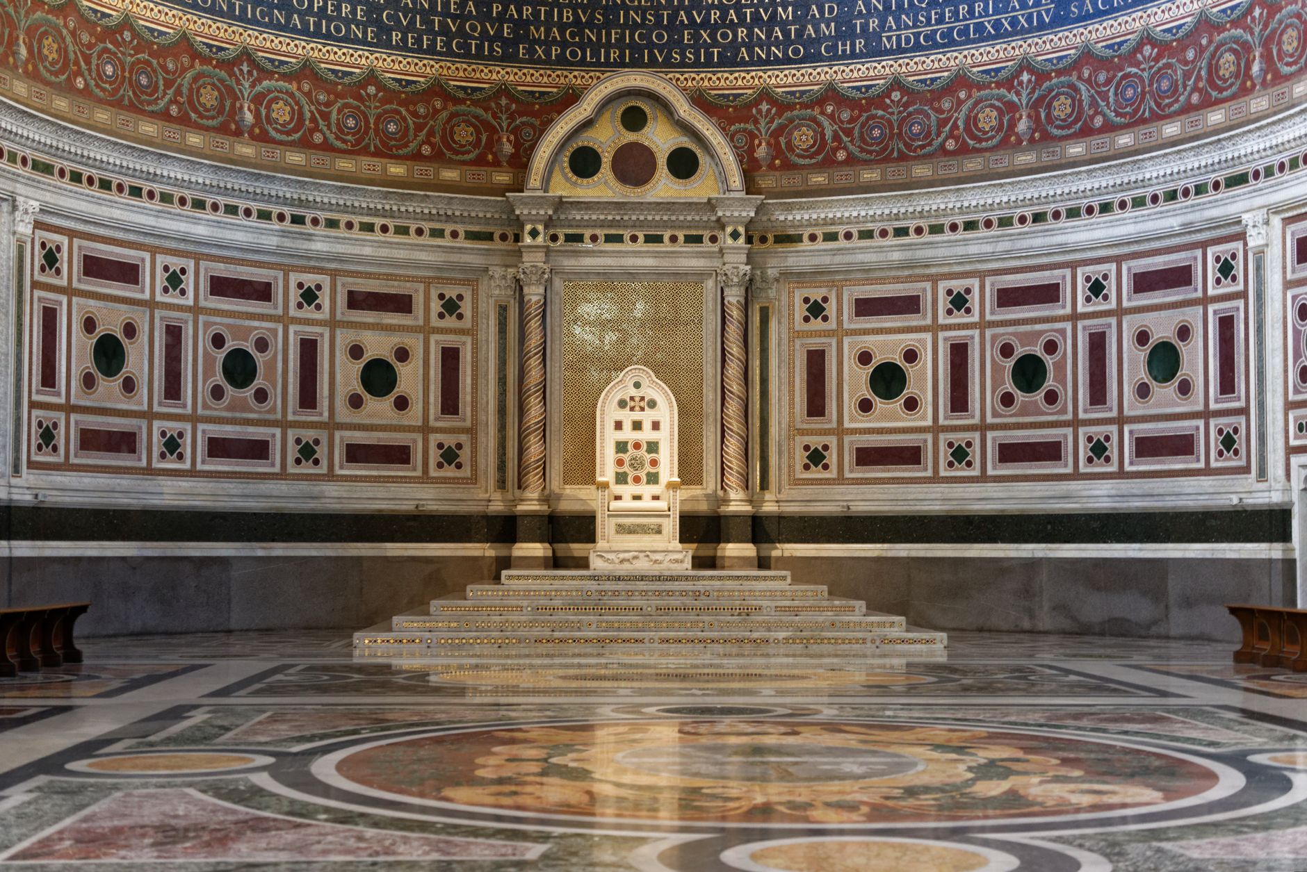 Ornate marble throne in grand hall with ornate patterns and reflections.