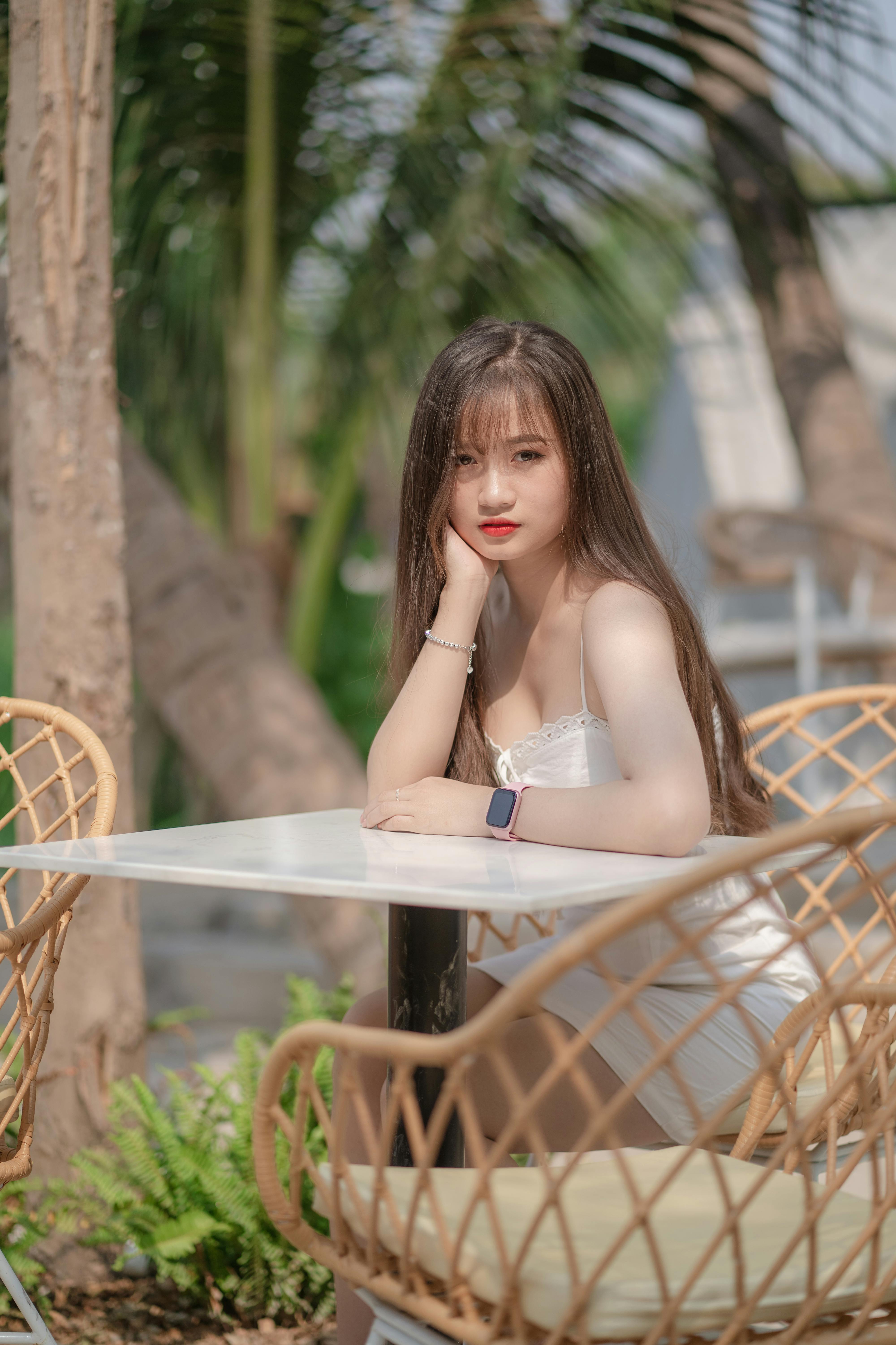 A young Asian woman with long hair posing at an outdoor cafe table in a garden setting.