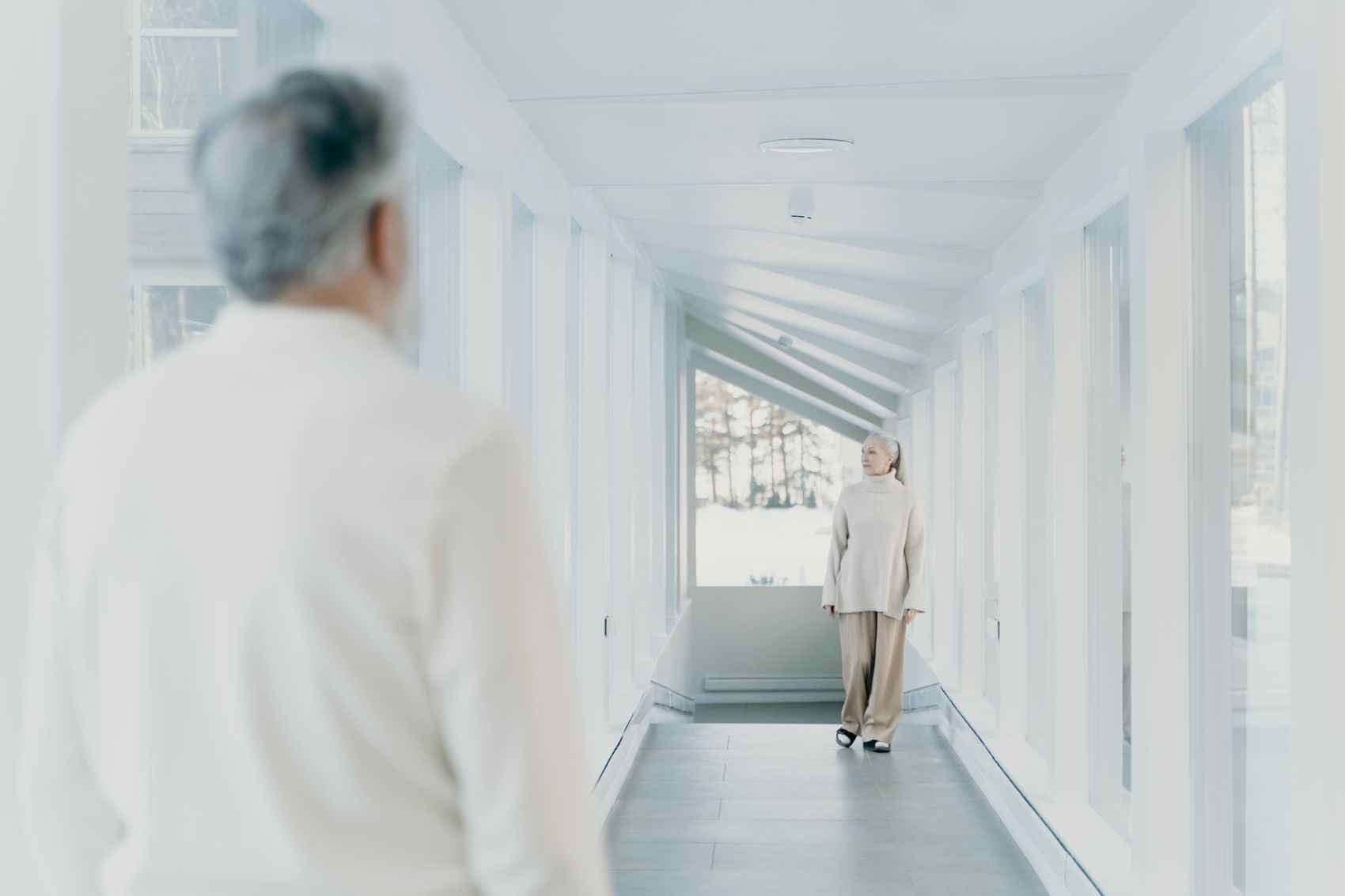 Two people walking comfortably through a well-lit modern hallway with large windows
