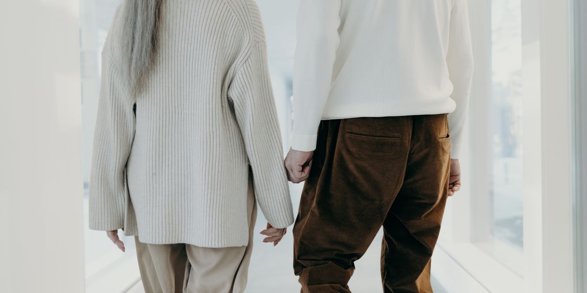 Casal de idosos caminhando de mãos dadas em corredor claro de casa — mobilidade segura