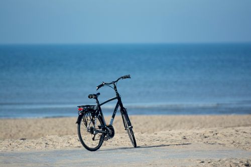 Free A solitary bicycle rests quietly on a sandy beach overlooking serene blue waters. Stock Photo