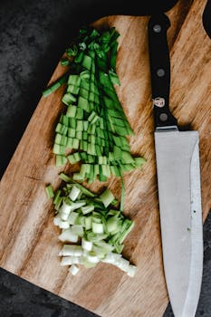 Freshly chopped green onions on a wooden cutting board with a knife, perfect for cooking inspiration.