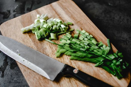 Sliced green onions neatly arranged on a cutting board with a knife, perfect for cooking themes.