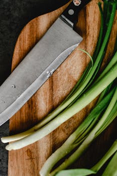 Close-up of fresh scallions and knife on a wooden chopping board for food preparation.
