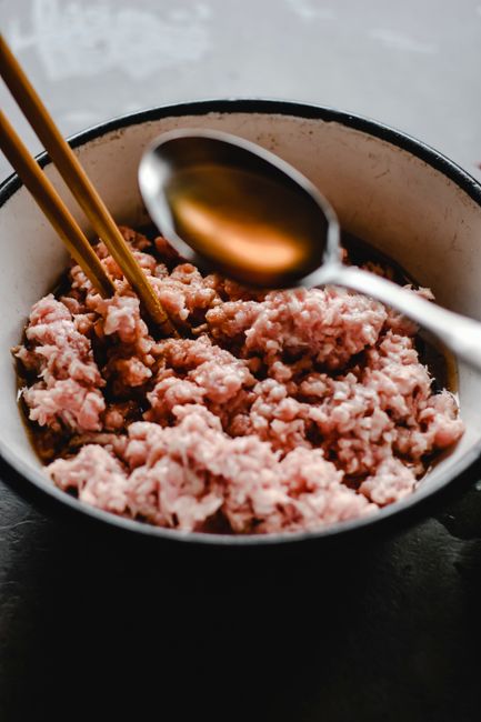 A block of frozen mince meat thawing in a glass bowl of cold water on a kitchen counter