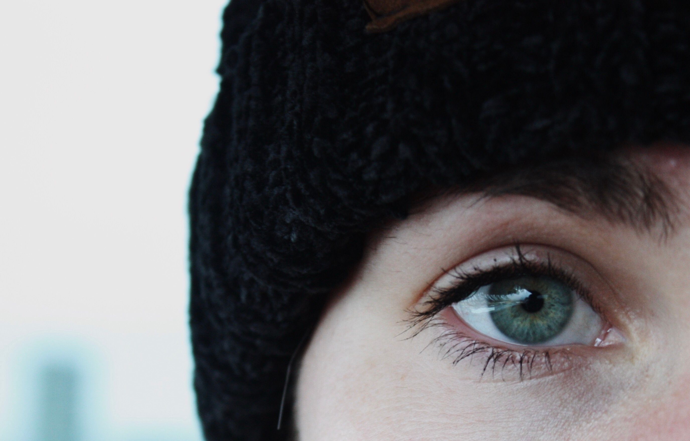 Detailed close-up of a woman's green eye, covered with a black beanie. Captivating and artistic.