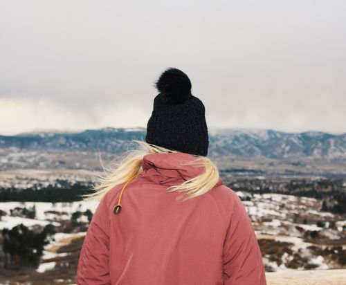 Free A woman in a pink jacket and beanie overlooks a snowy mountain landscape. Stock Photo