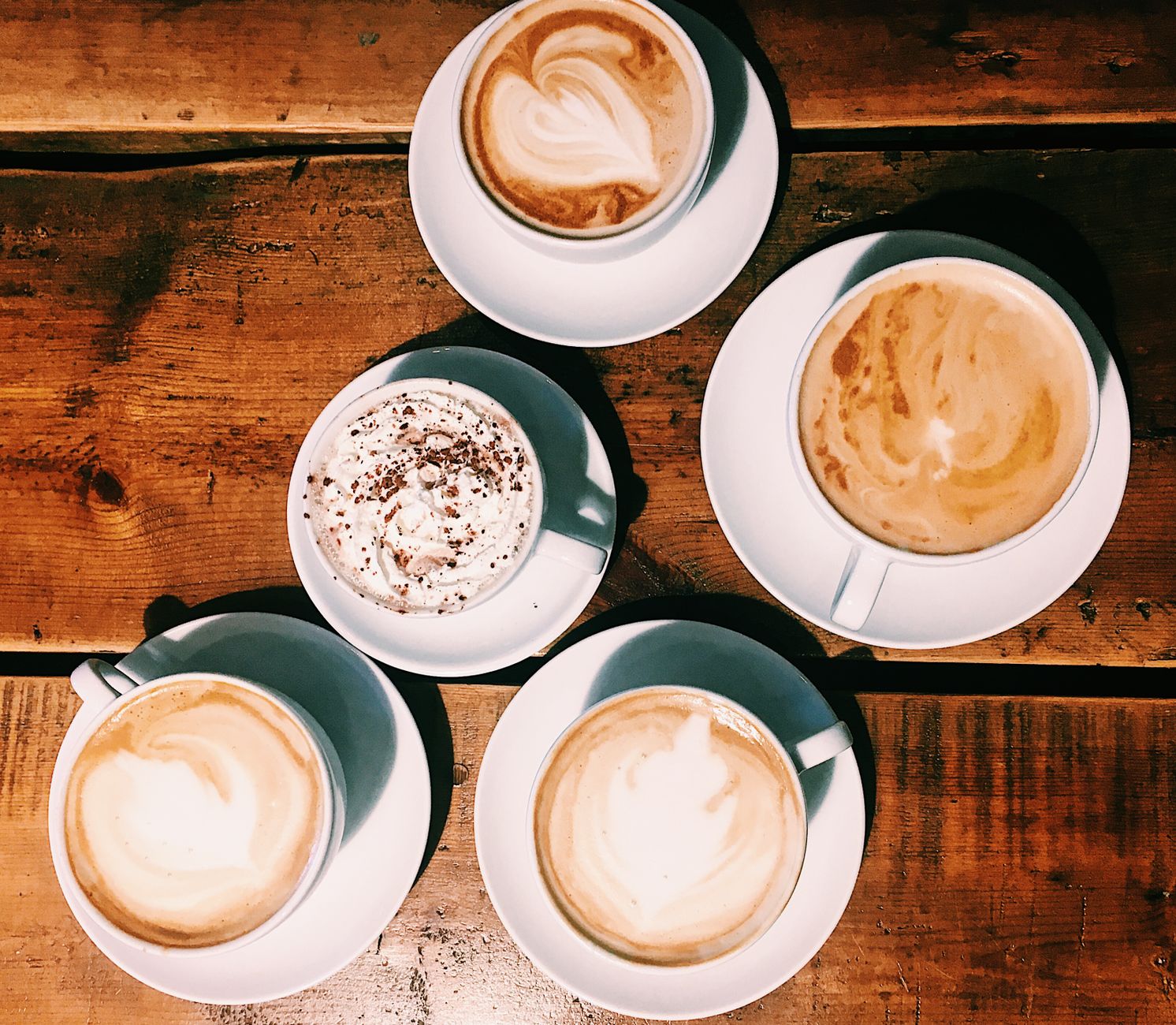 A top-down view of various lattes and cappuccinos with latte art on a wooden table.