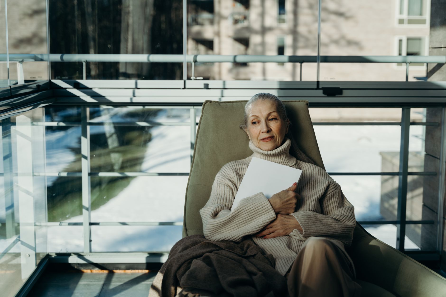 Longevity research book — Elderly woman in cozy sweater relaxes indoors with a book in a serene setting.