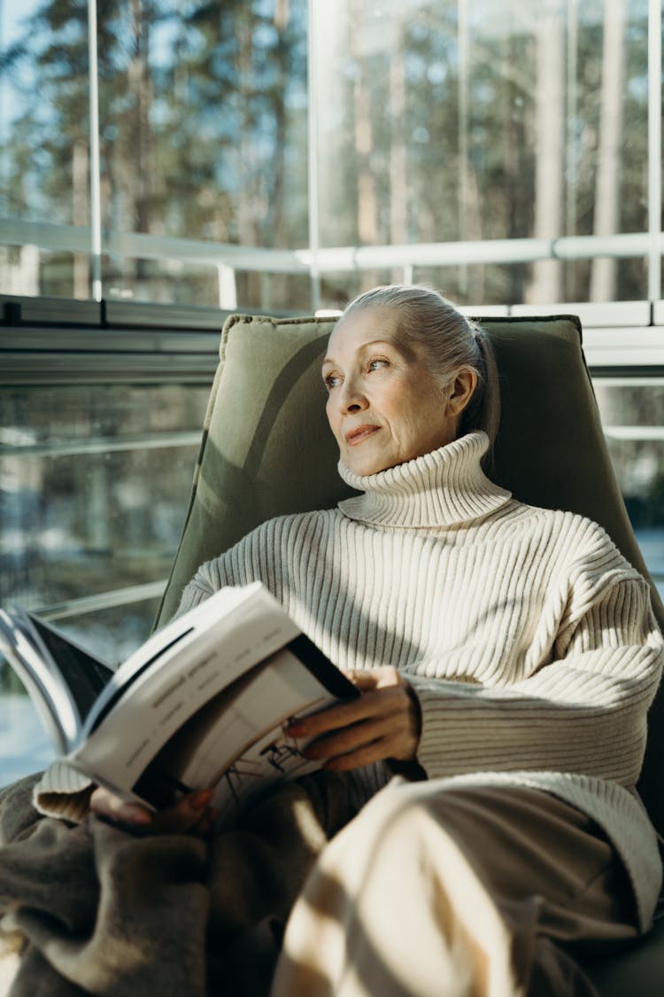 A Woman Holding A Magazine While Sitting On A Chair