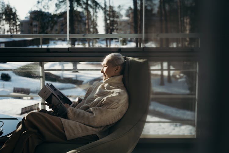 A Woman Reading A Magazine By The Window