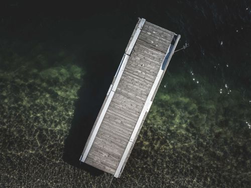 Free Drone view of wooden pier near coast of clear calm sea on sunny day Stock Photo