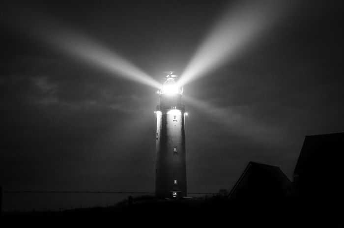 Lighthouse beams cutting through night in monochrome — photo by ClickerHappy on Pexels