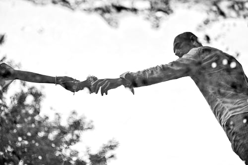 Grayscale Photo of  a Man Reaching for the Flowers on a Woman's Hand