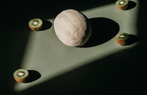 Melon and Sliced Kiwis on Green Surface