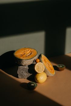 A creative still life with melons, lemon, and kiwi in natural light.