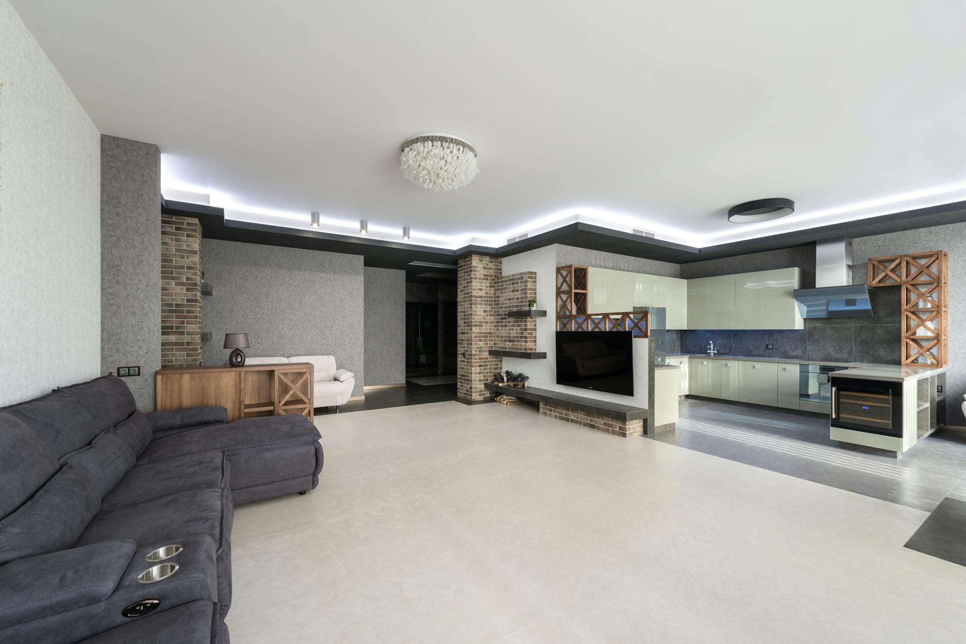 Kitchen with cupboards and modern appliances placed near living room with TV and comfortable gray couch in light stylish apartment