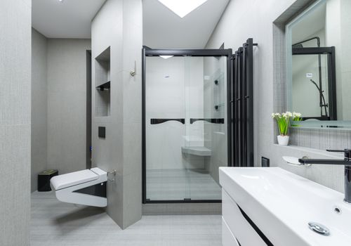 Sink with tap placed at wall with mirror in light spacious bathroom with toilet and glass shower cabin in apartment