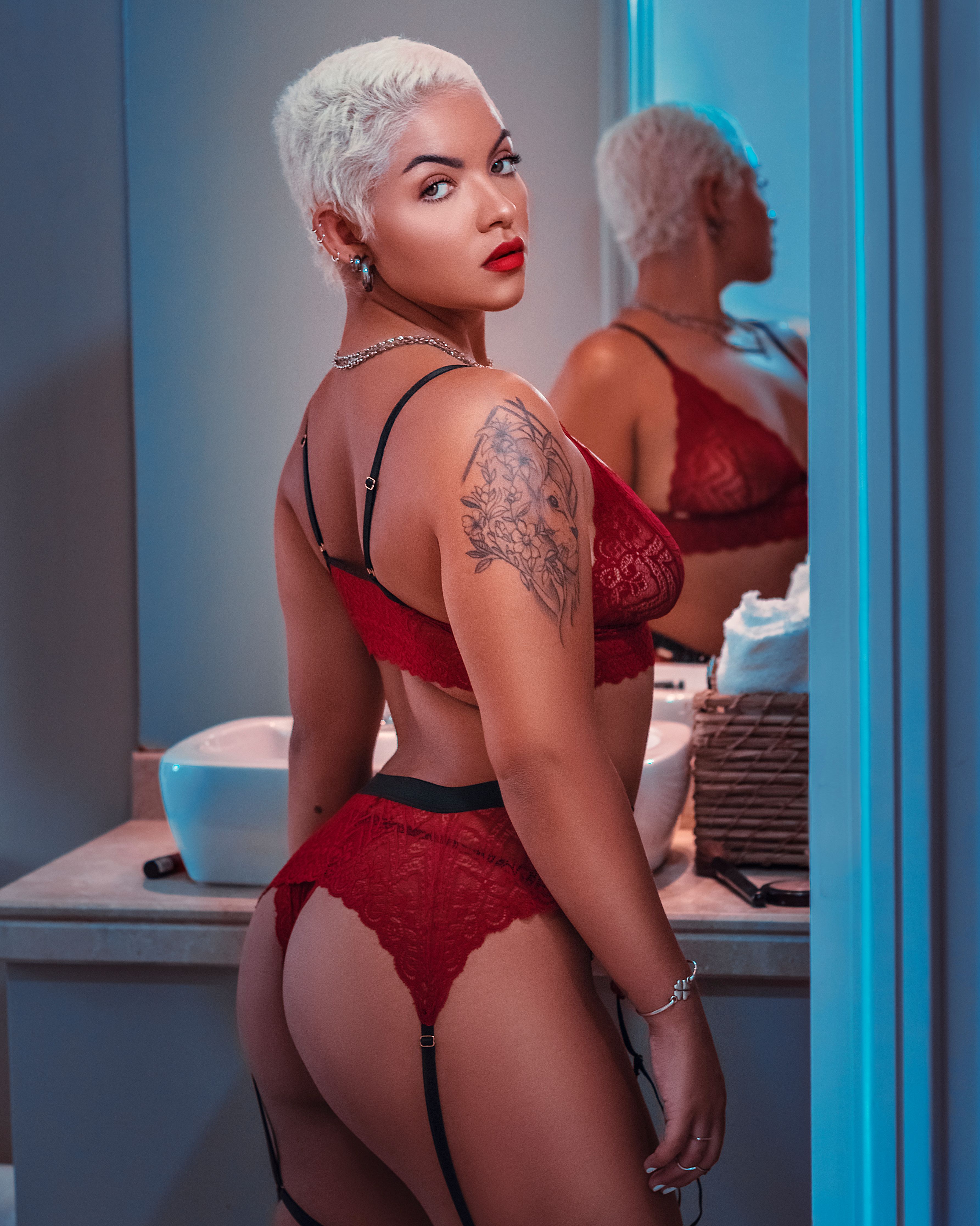 Elegant and alluring portrait of a confident woman in red lace lingerie, showcasing tattoos in an intimate setting.