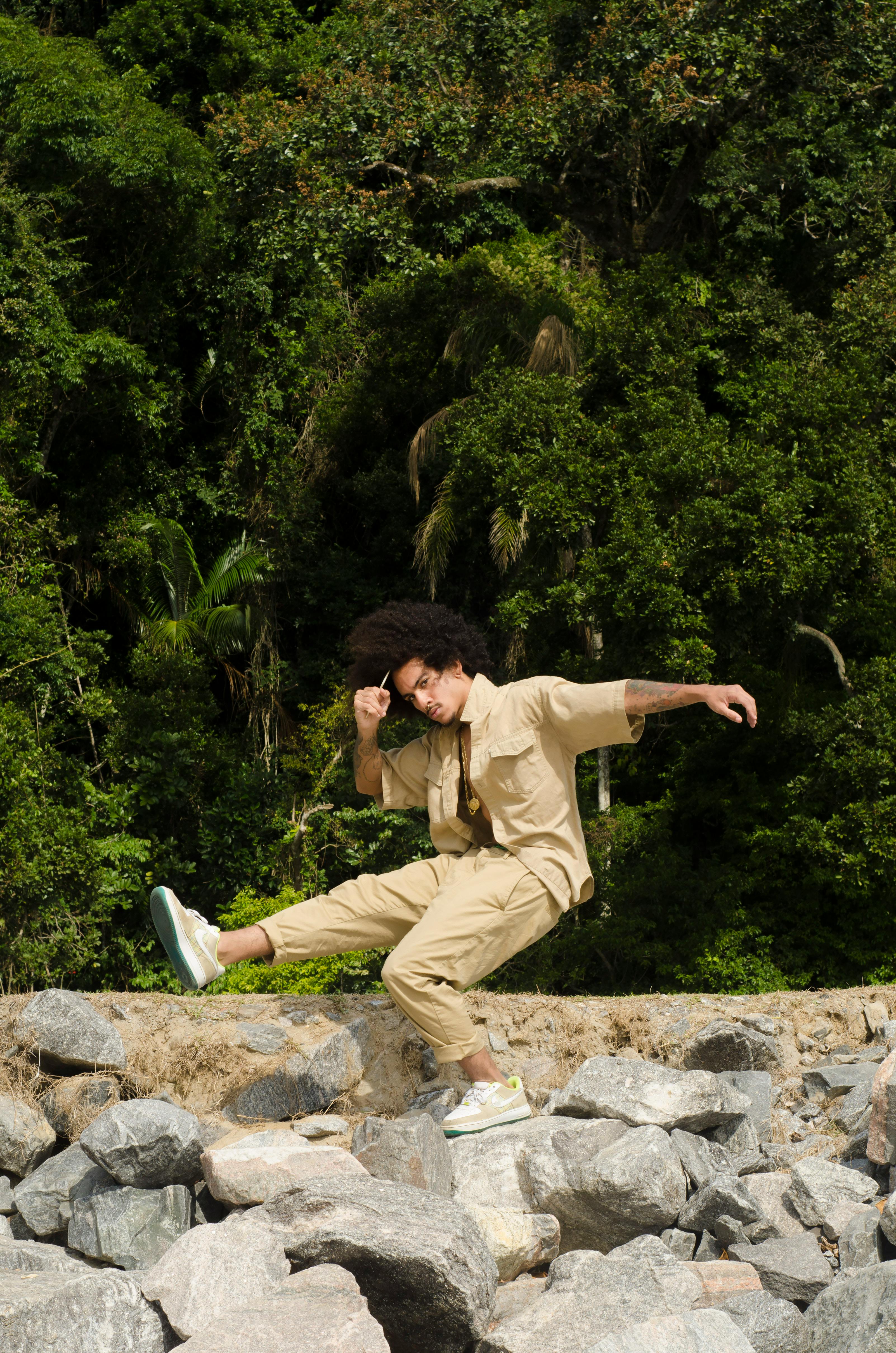 A man performs a dynamic pose on rocks amidst lush green forest.