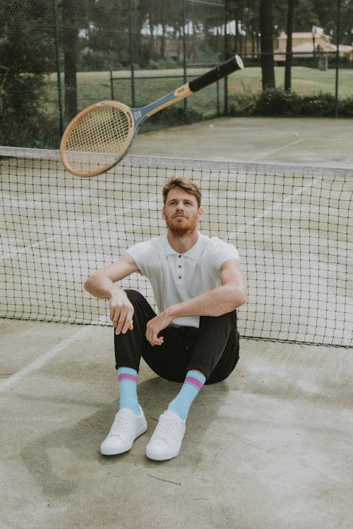 Free Man in White Polo Shirt and Black Pants Sitting on Tennis Court Stock Photo