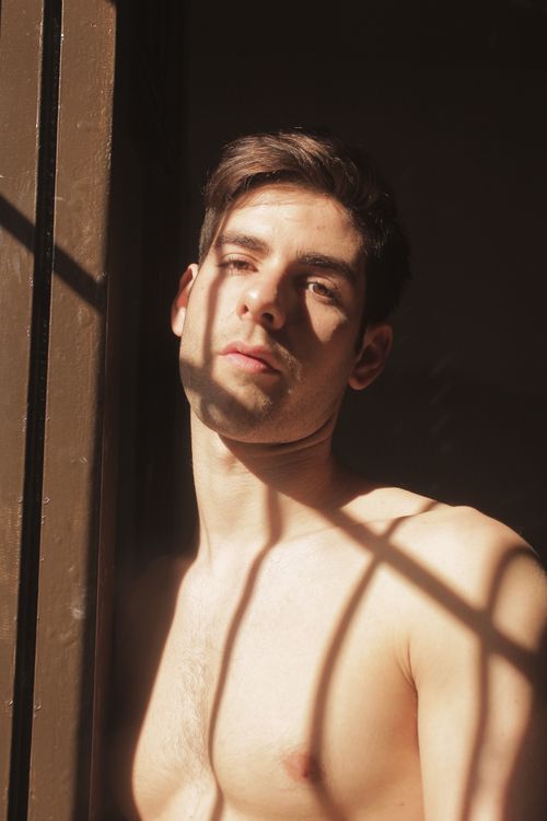 Free A captivating portrait of a shirtless man standing indoors with dramatic natural lighting and shadows. Stock Photo