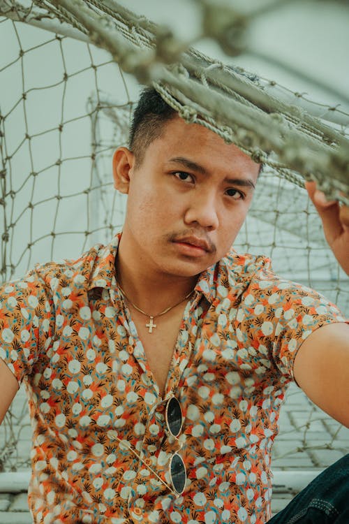 Self assured ethnic male with mustache in shirt and sunglasses sitting under net and looking at camera