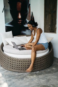 Young woman in casual wear working on laptop with headphones, relaxing indoors.