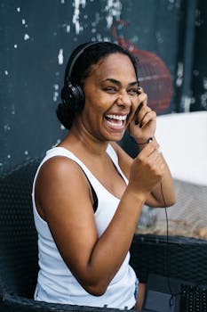Happy woman in a white tank top enjoying music on headphones while smiling brightly.